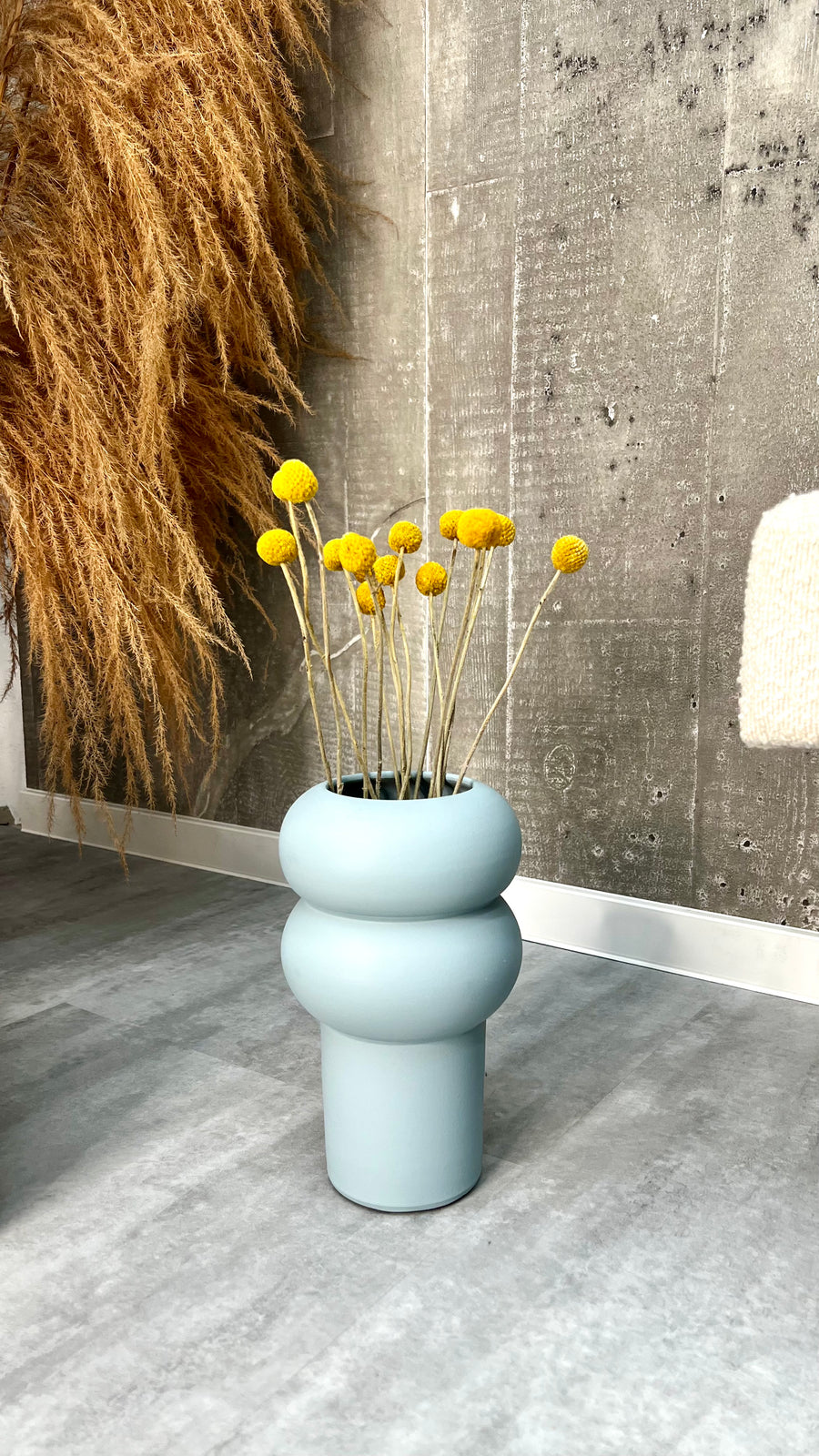 Keramikvase Ripple Hellblau mit gelben Trockenblumen vor Betonwand – skandinavische Wohndeko